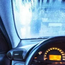 The view from inside a car through a foggy, rain-streaked windshield with the dashboard and steering wheel in the foreground.