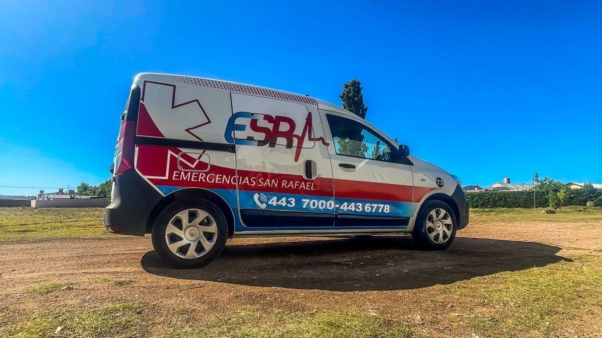 Una furgoneta médica de emergencia de la ESA, de color blanco y rojo, aparcada en un campo de tierra bajo un cielo azul despejado.