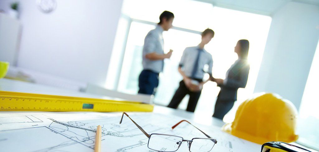 A group of people are standing around a table with a hard hat and glasses on it.