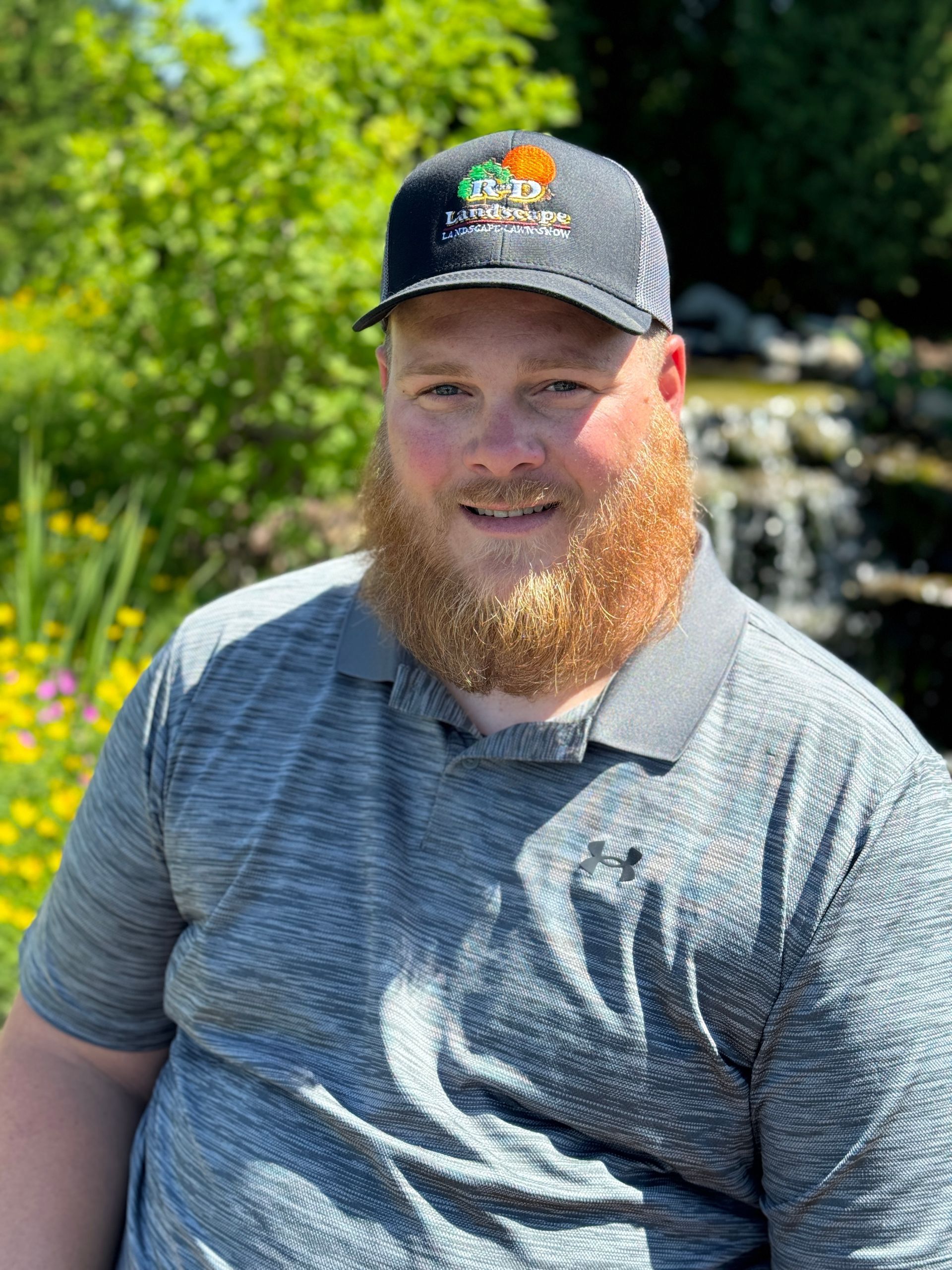 A man with a beard is wearing a hat and a gray shirt.