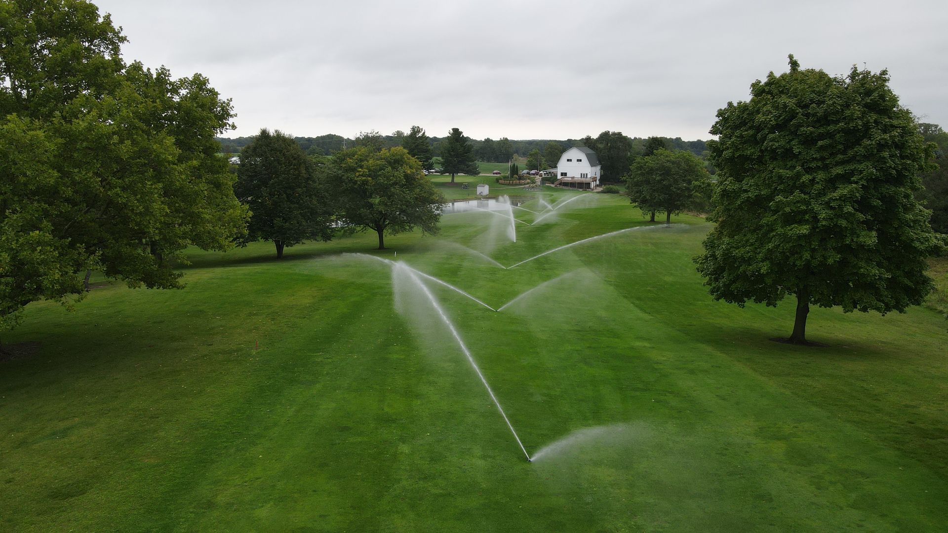 An aerial view of a sprinkler spraying water on a lush green field.