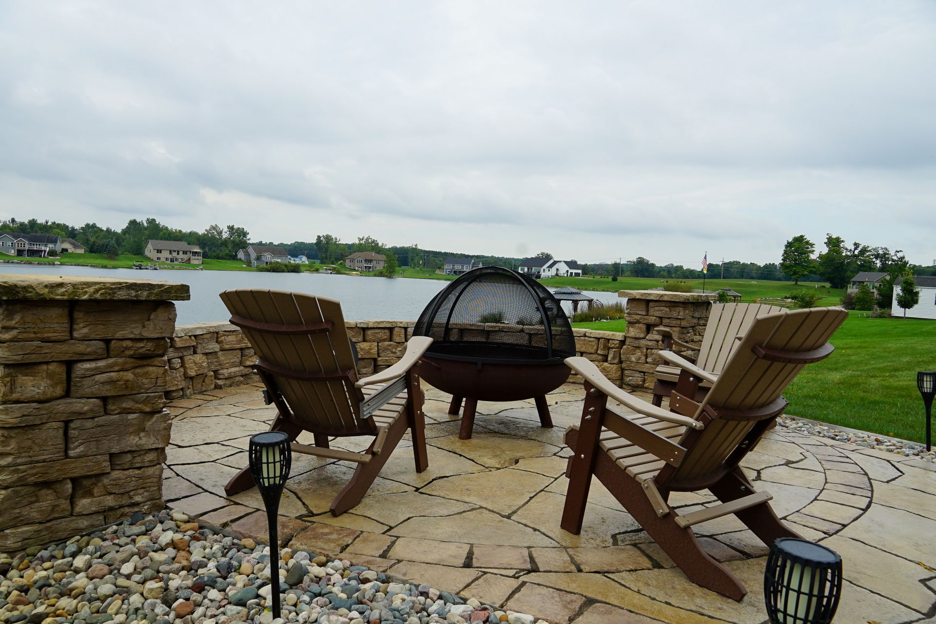 A patio with chairs and a fire pit overlooking a lake.
