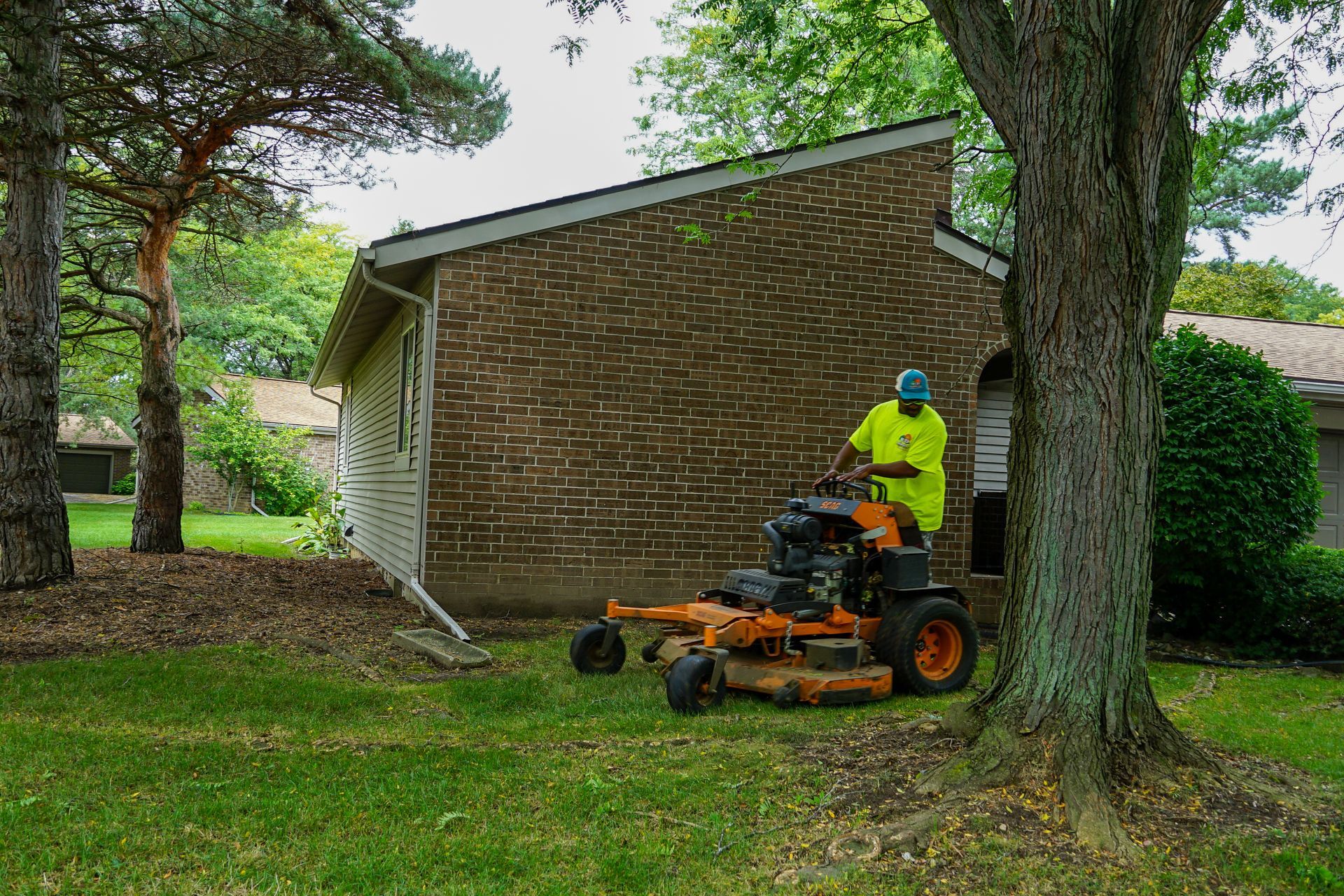 A man is riding a lawn mower in front of a brick house.
