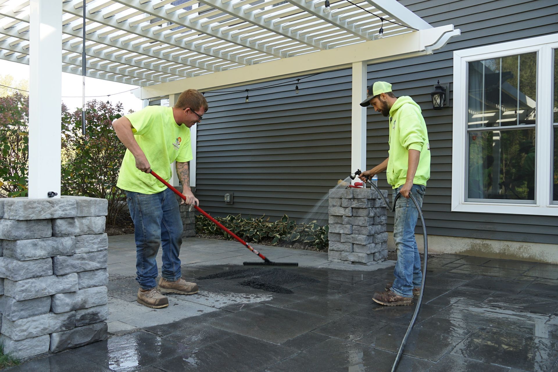 Two men are working on a patio in front of a house.