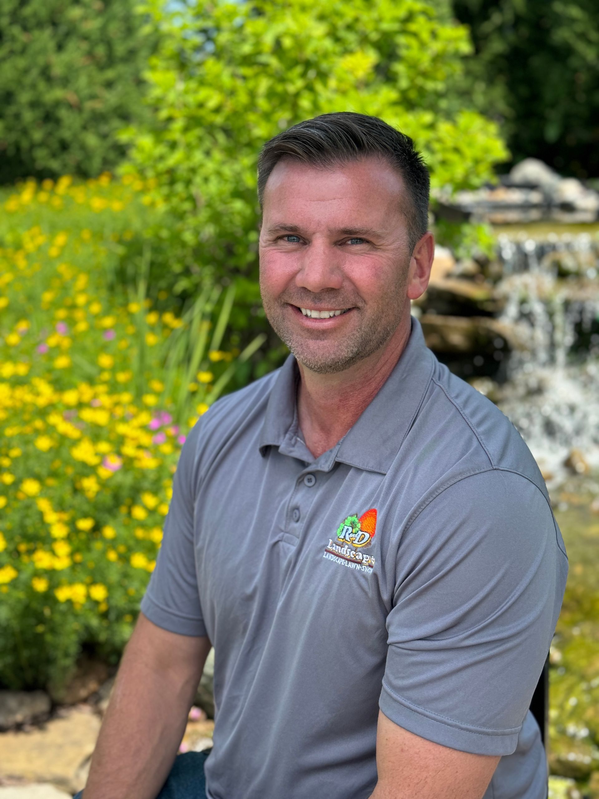 A man is sitting in front of a waterfall in a garden.