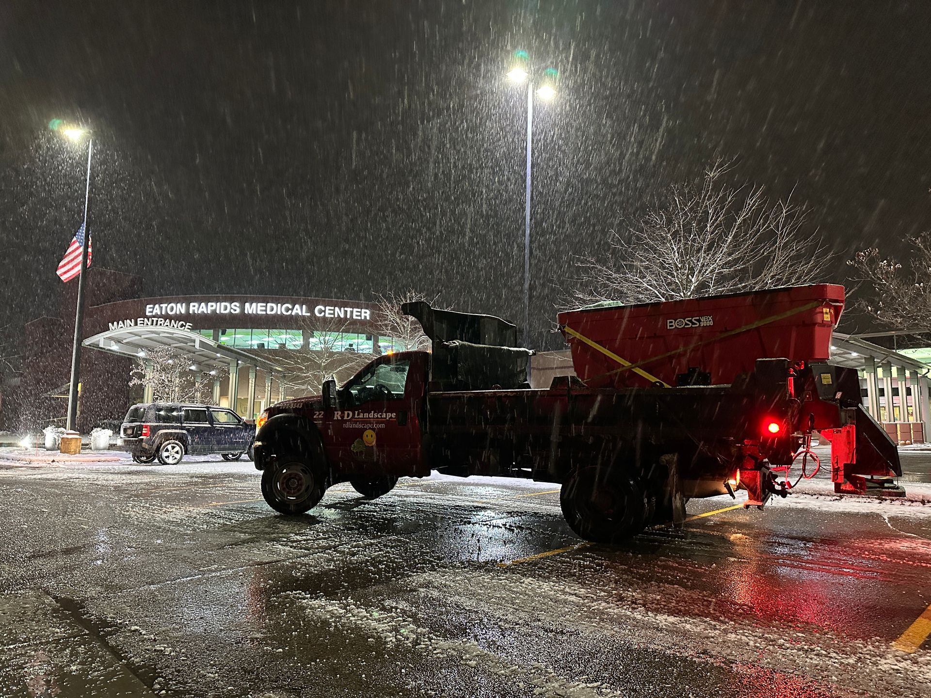 A snow plow is parked in a parking lot at night.