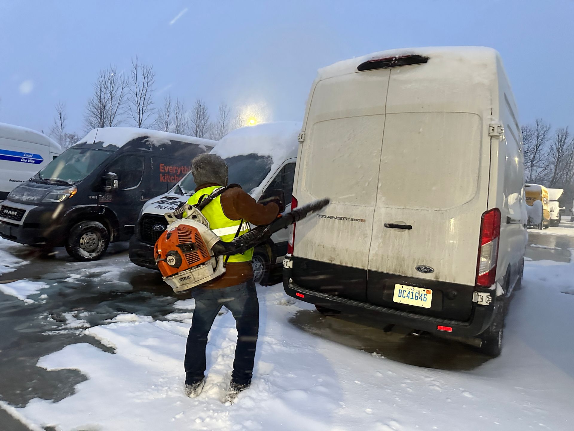 A man is using a snow blower to clear snow from a parking lot.