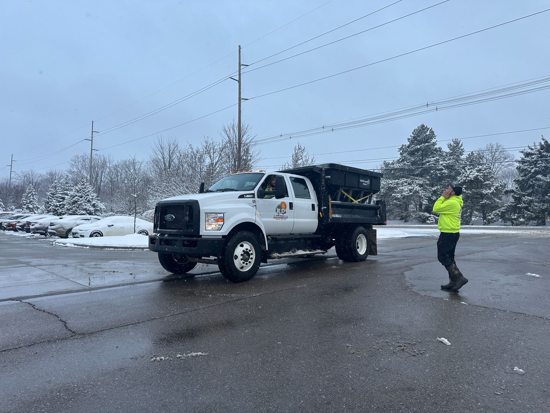 A man in a yellow jacket is standing next to a truck in a parking lot.