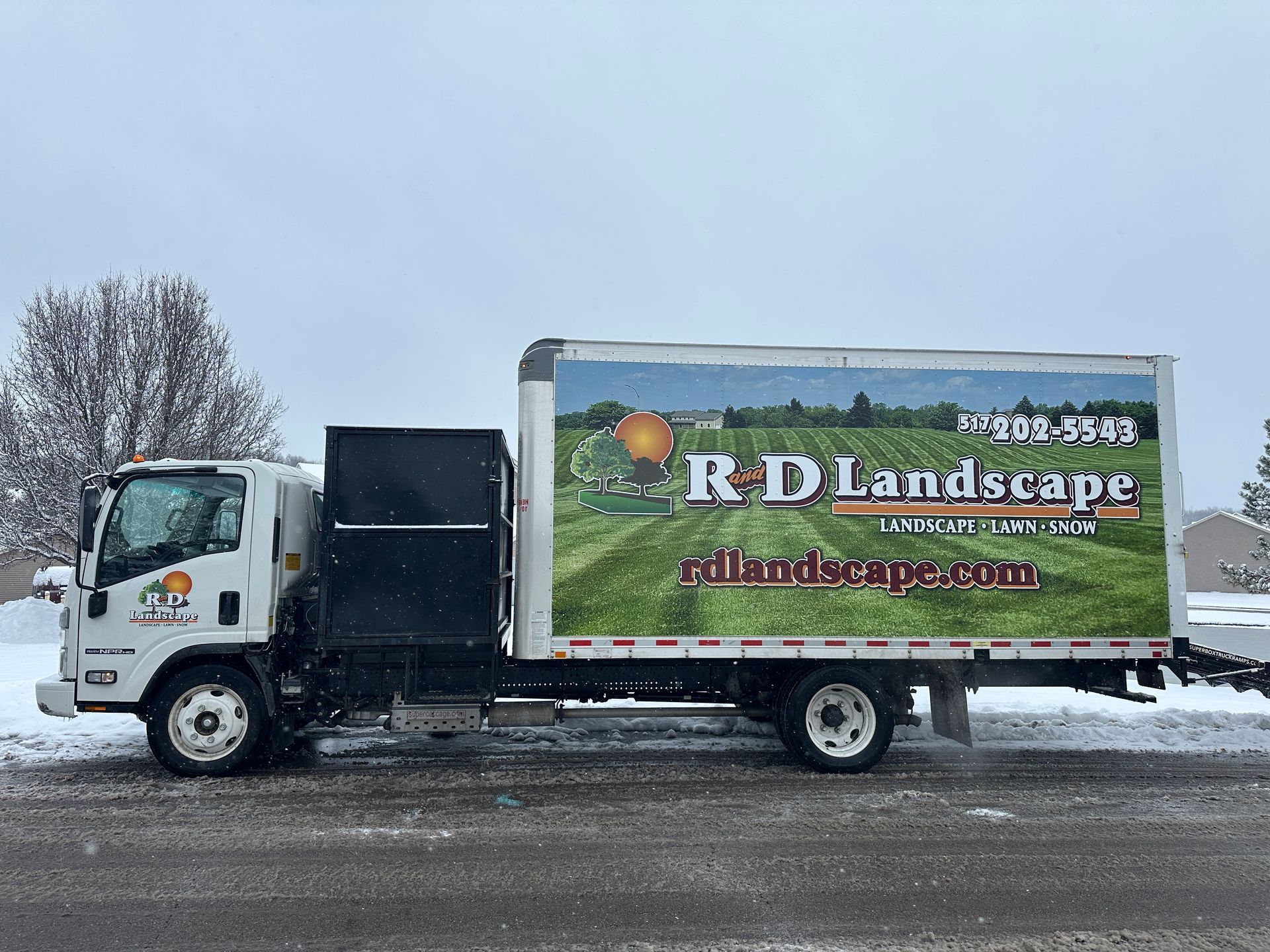 A landscape truck is parked on the side of the road in the snow.