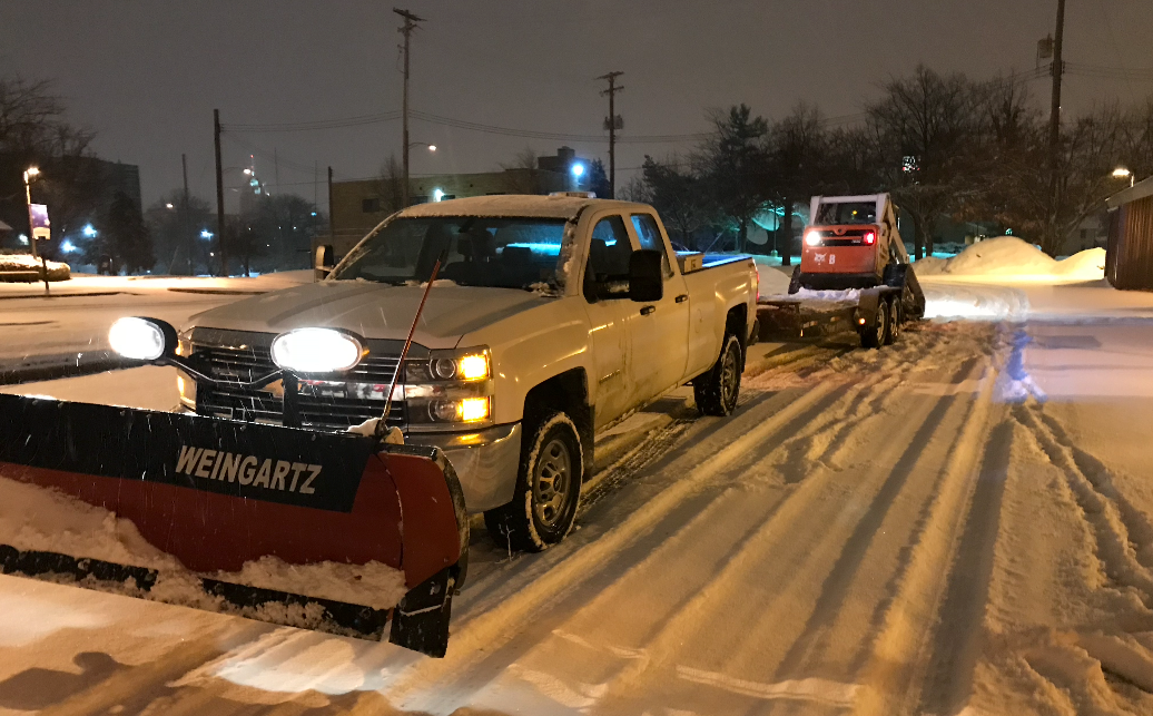 A snow plow is plowing a snowy road at night.