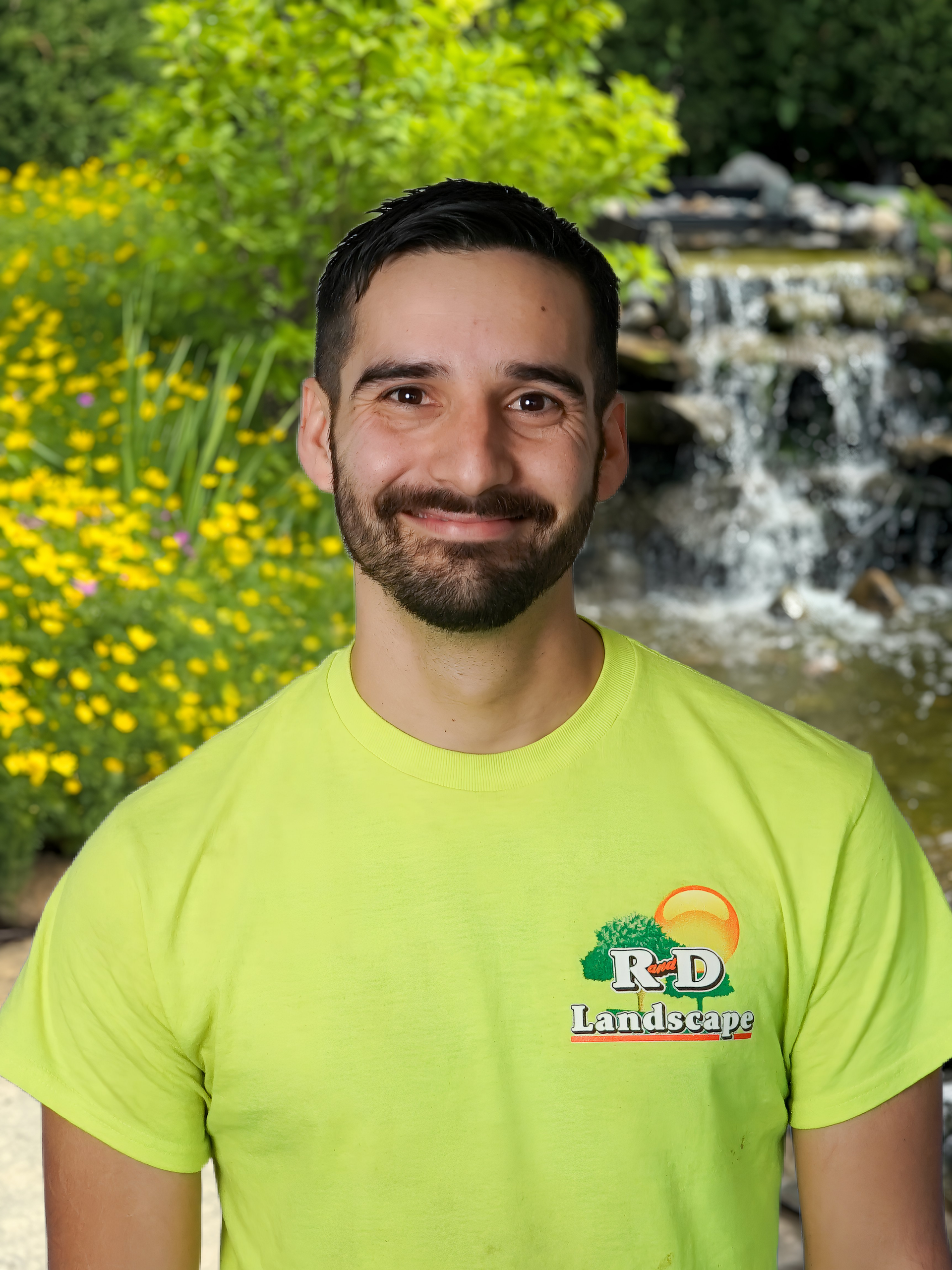 A man wearing a hat and glasses is sitting in front of a waterfall.