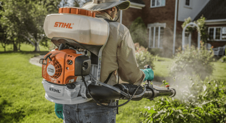 A man is spraying a lawn with a stihl backpack sprayer.