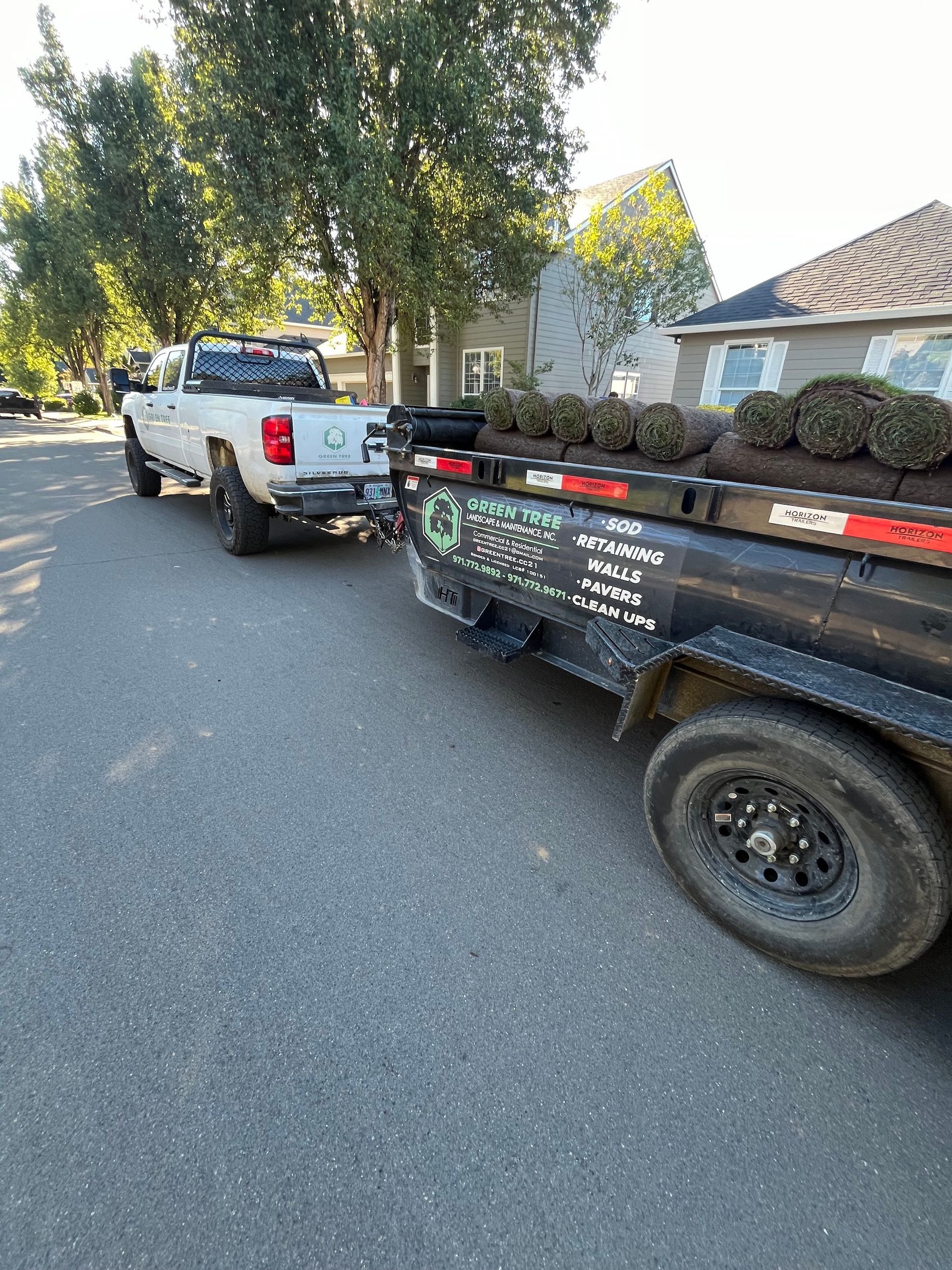 A truck is towing a trailer full of plants down a street.