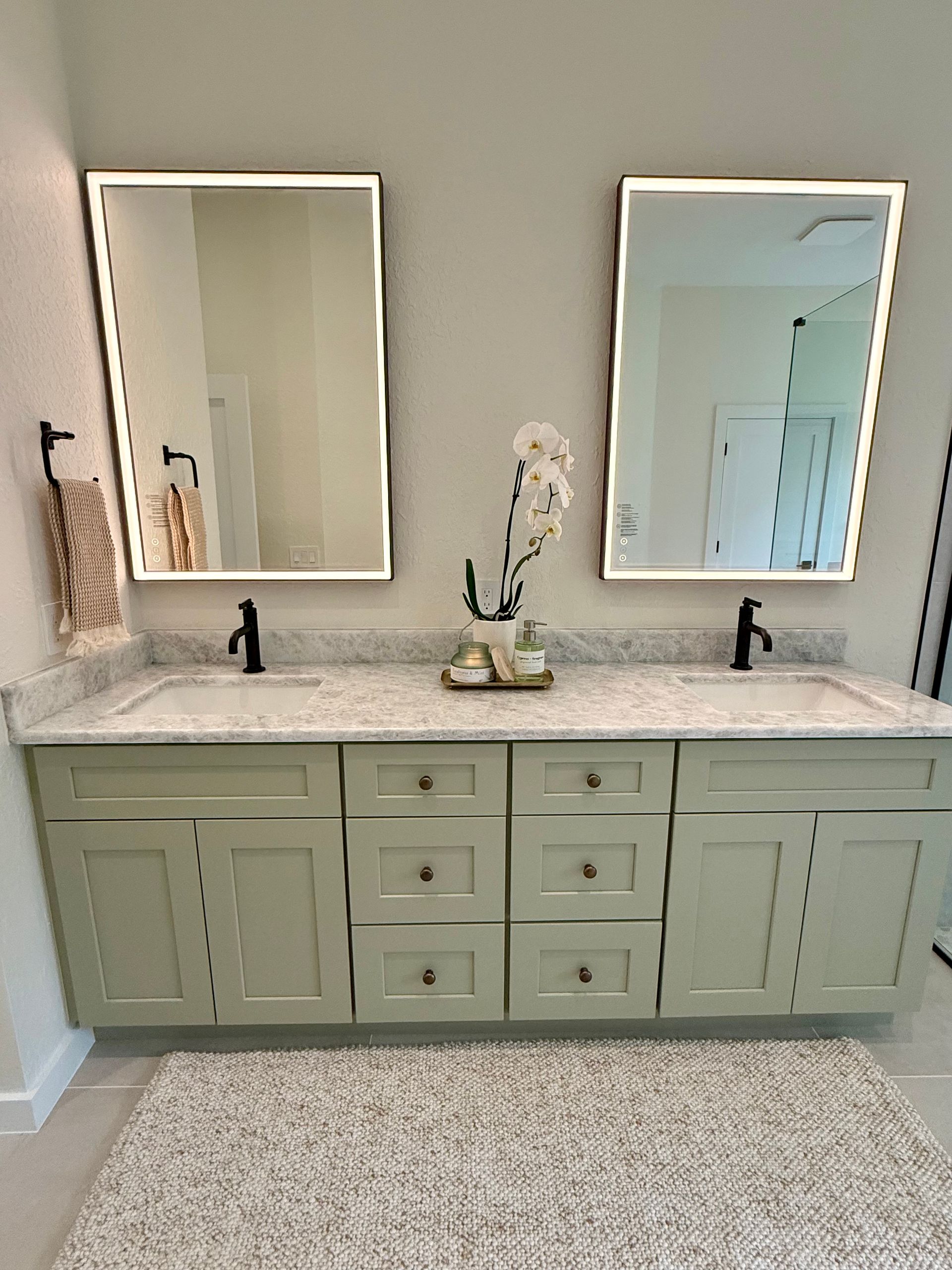 Double vanity bathroom with sage green cabinets, white countertops, and two mirrors