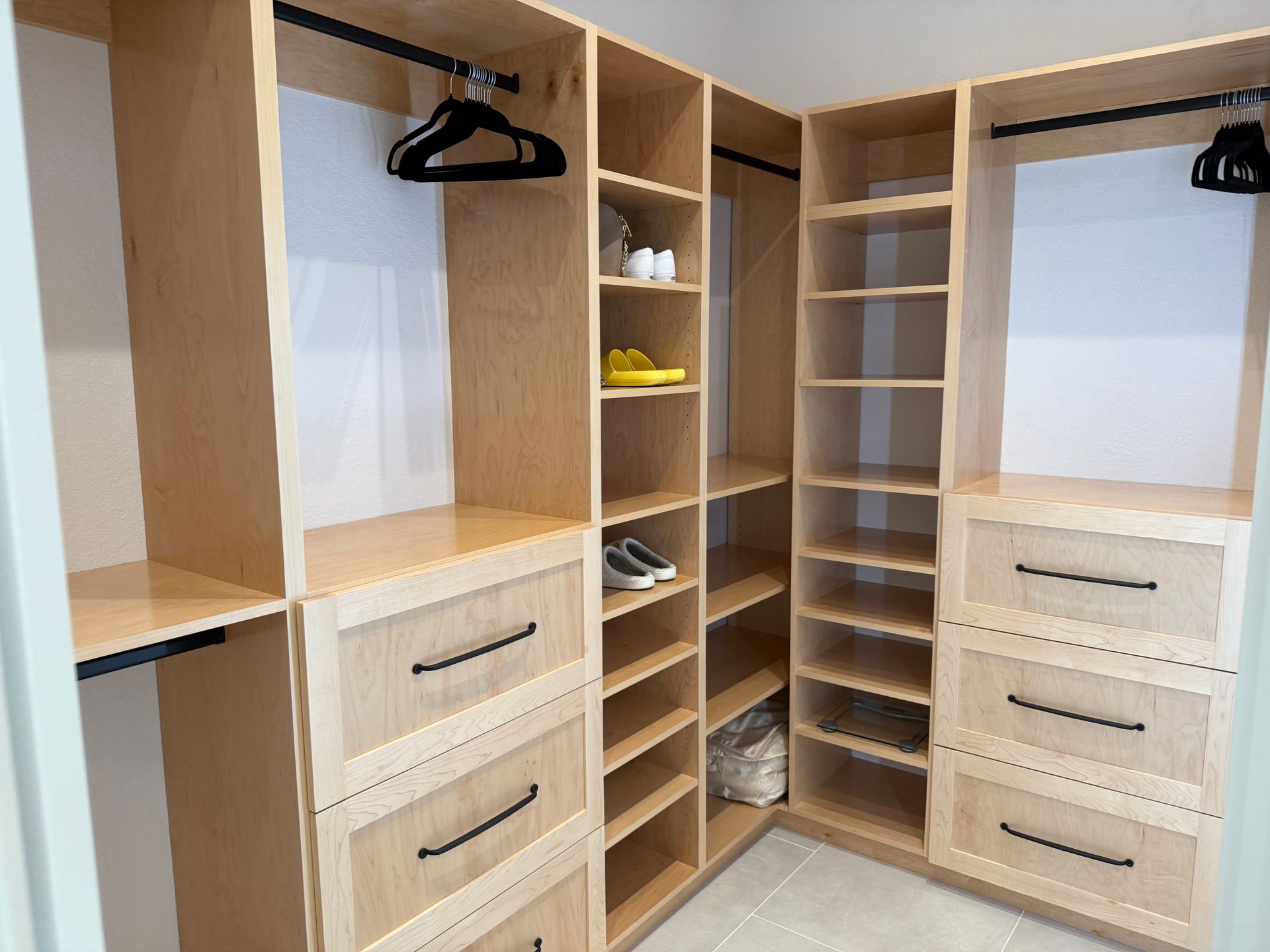 Built-in wooden walk-in closet with open shelves, drawers, and hanging rods in a bright room