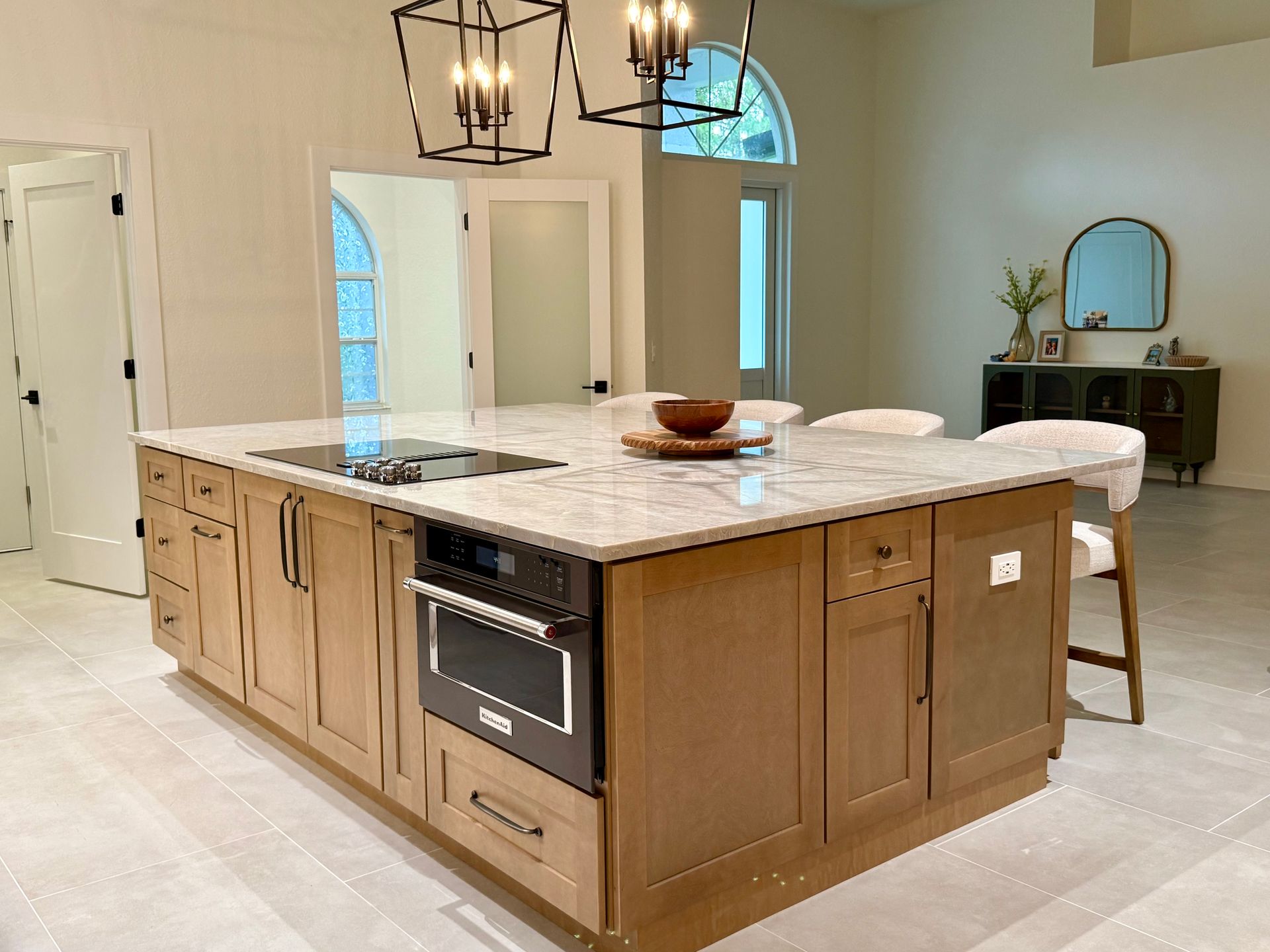 Spacious kitchen with a large marble island, wood cabinetry, pendant lights, and a stool by the counter.
