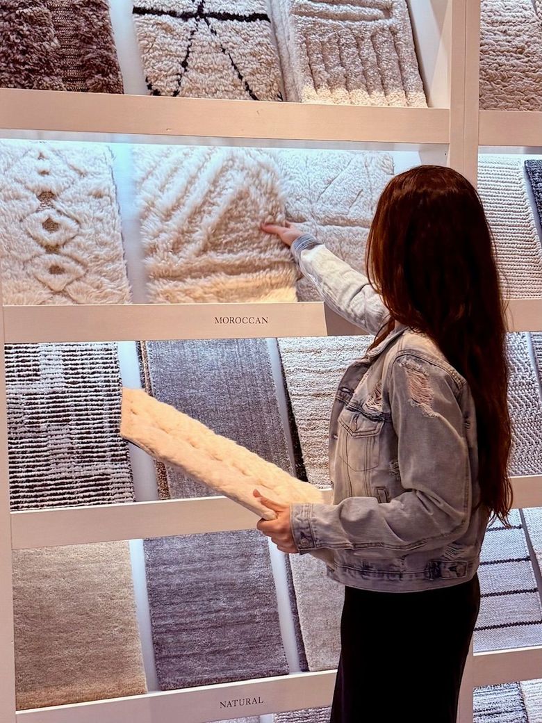 Woman in denim jacket pointing at textured wall samples in a showroom