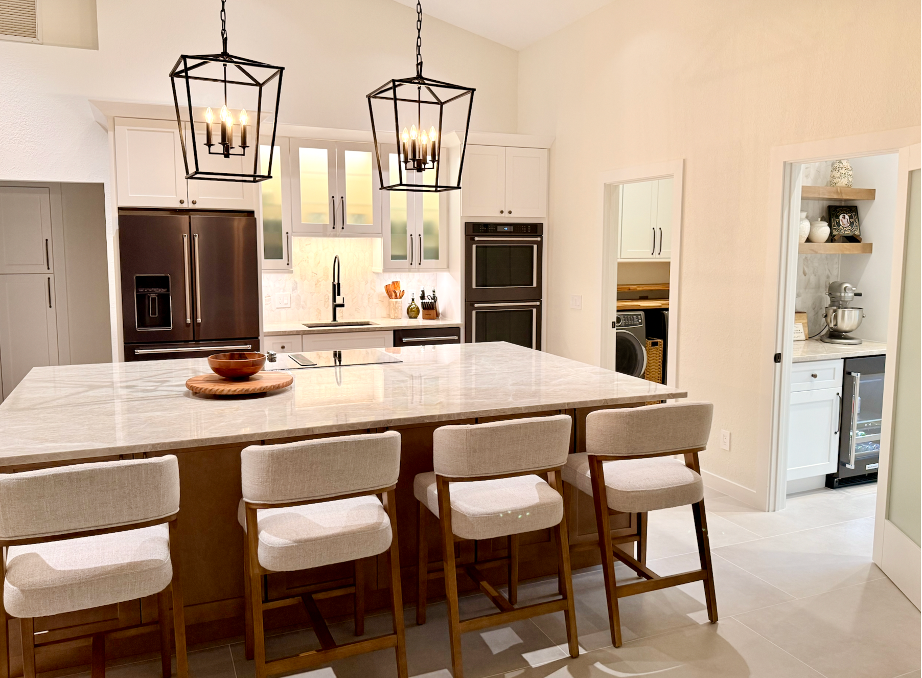 Bright modern kitchen with marble island, cushioned stools, pendant lights, and stainless steel appliances