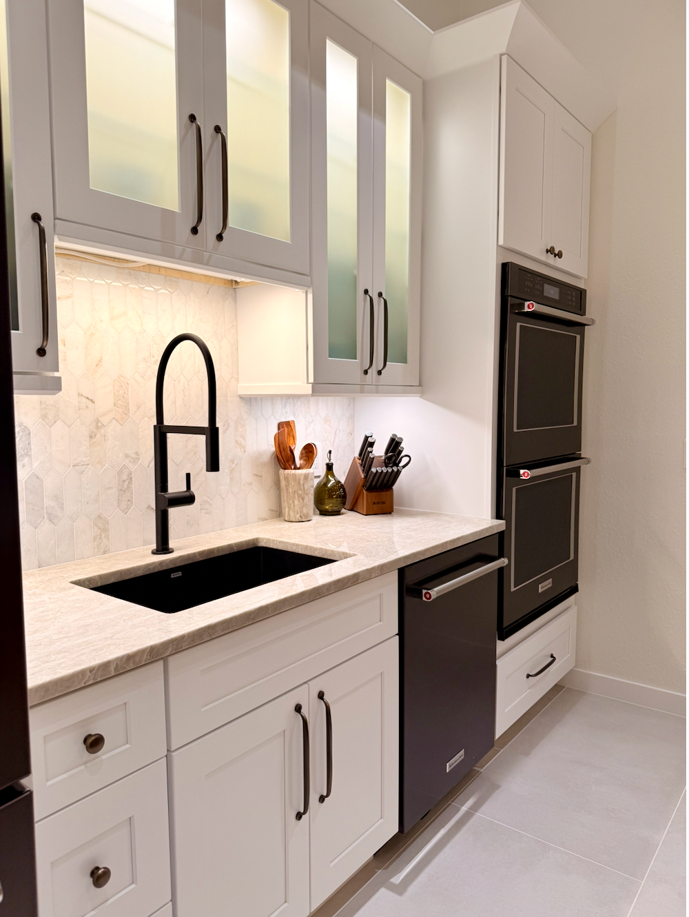 Bright modern kitchen with white cabinets, black sink faucet, and built-in oven.