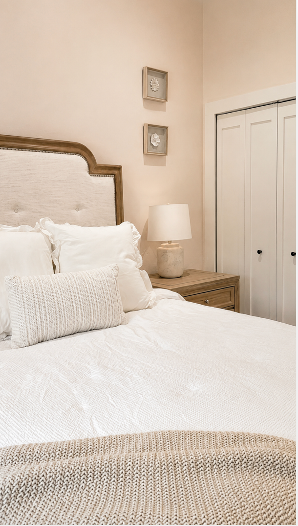 Cozy bedroom with a white bed, beige headboard, nightstand lamp, and closet doors.