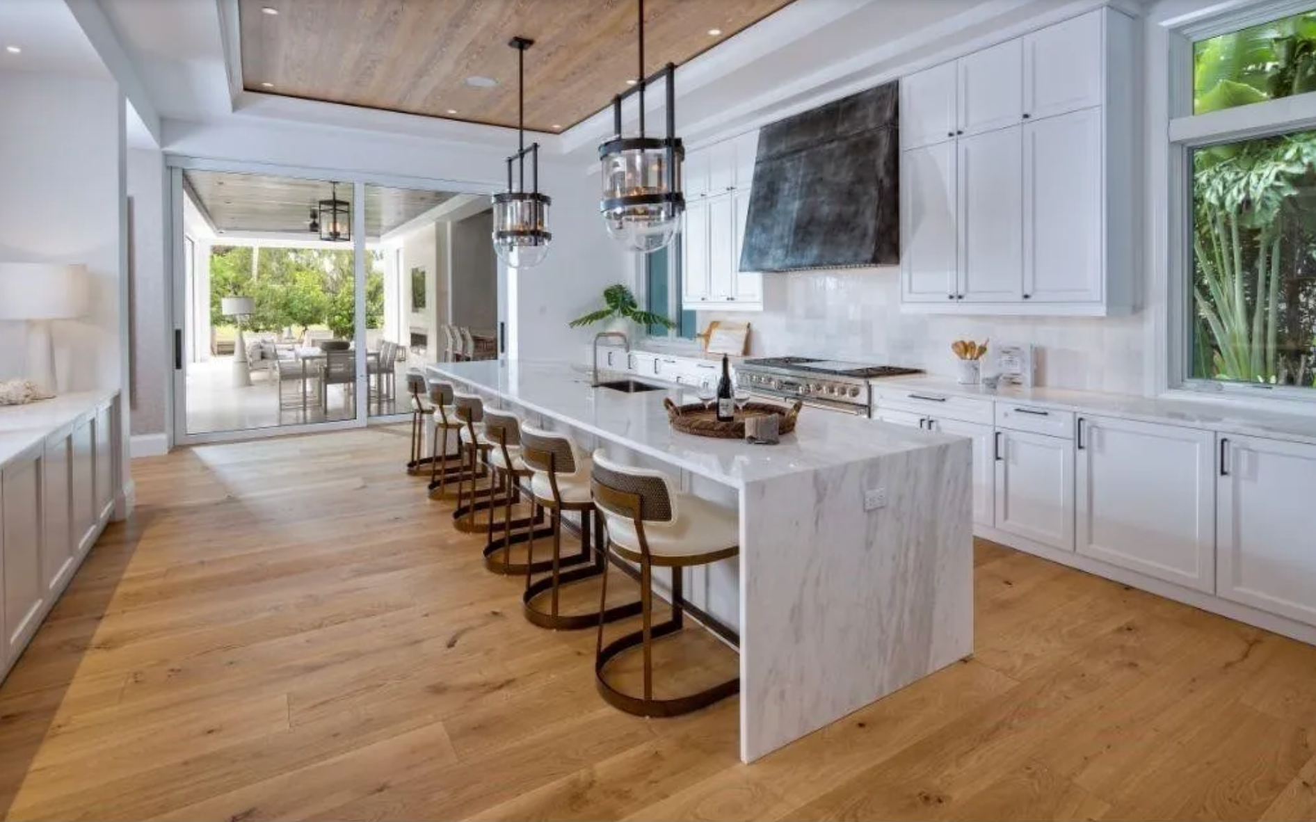 Bright modern kitchen with marble island, barstools, white cabinets, and wood floors