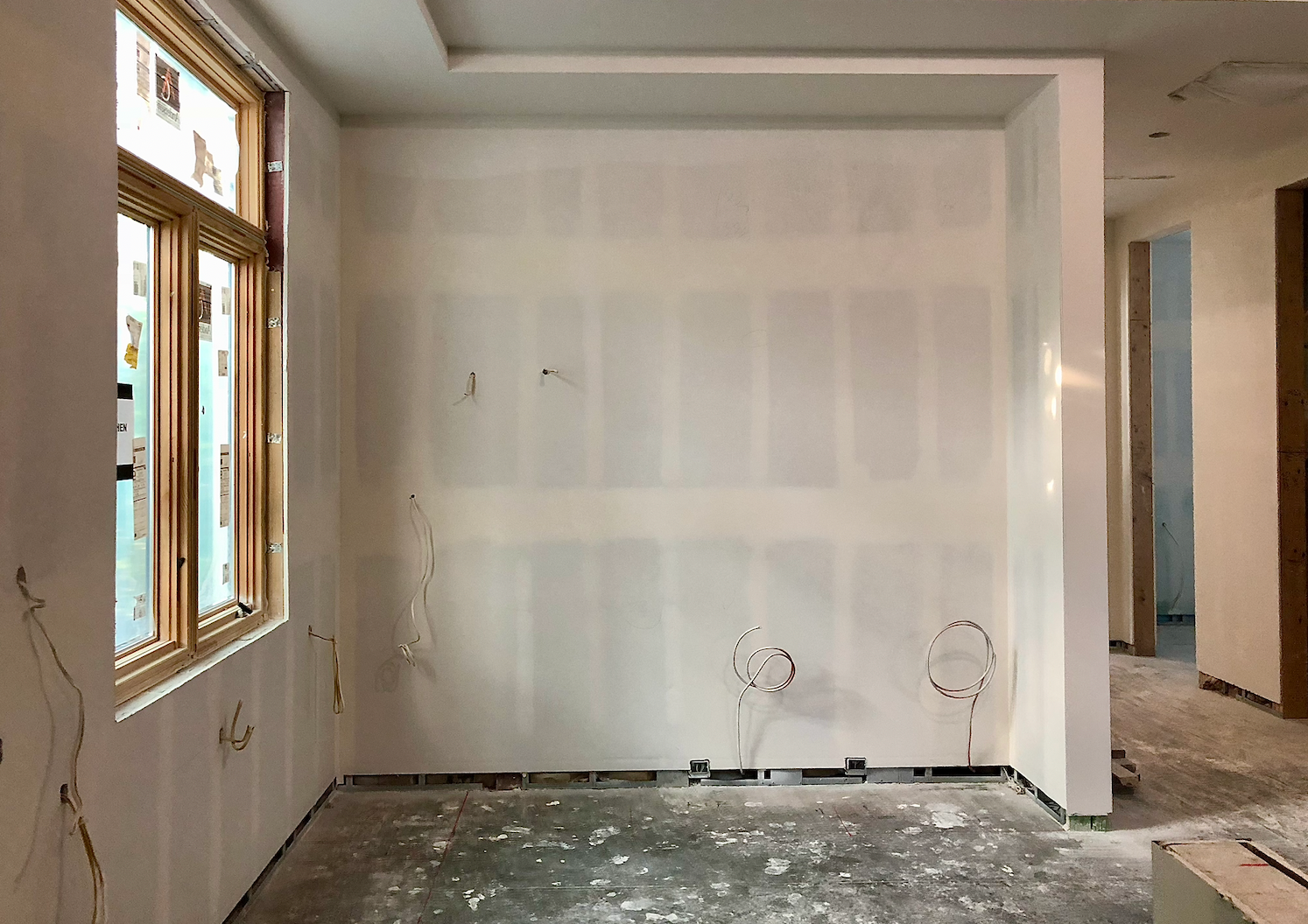 Unfinished room with drywall, a large window, exposed wiring, and a floor covered in construction debris.
