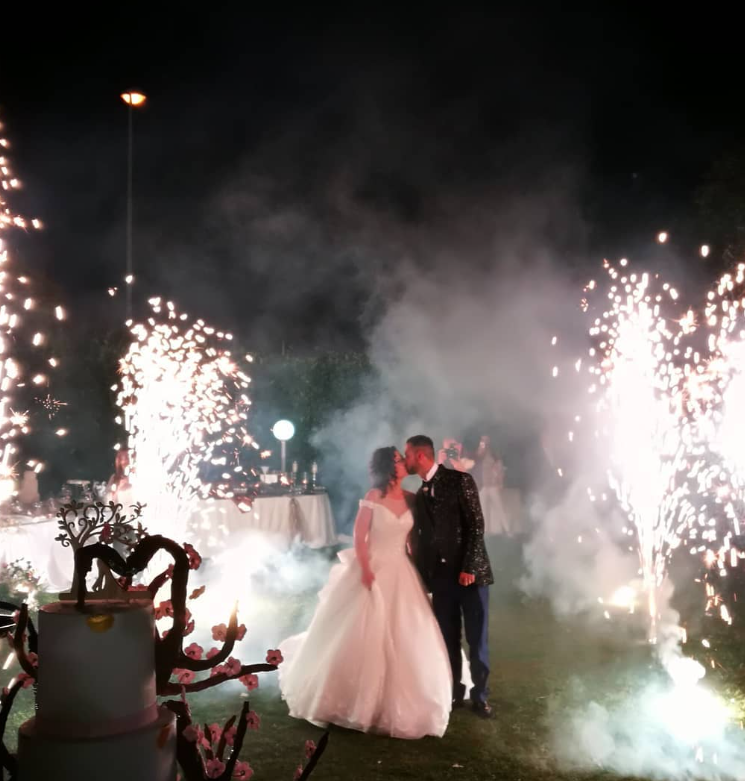 Coppia che si bacia tra fuochi d'artificio e fumo durante un ricevimento di nozze.