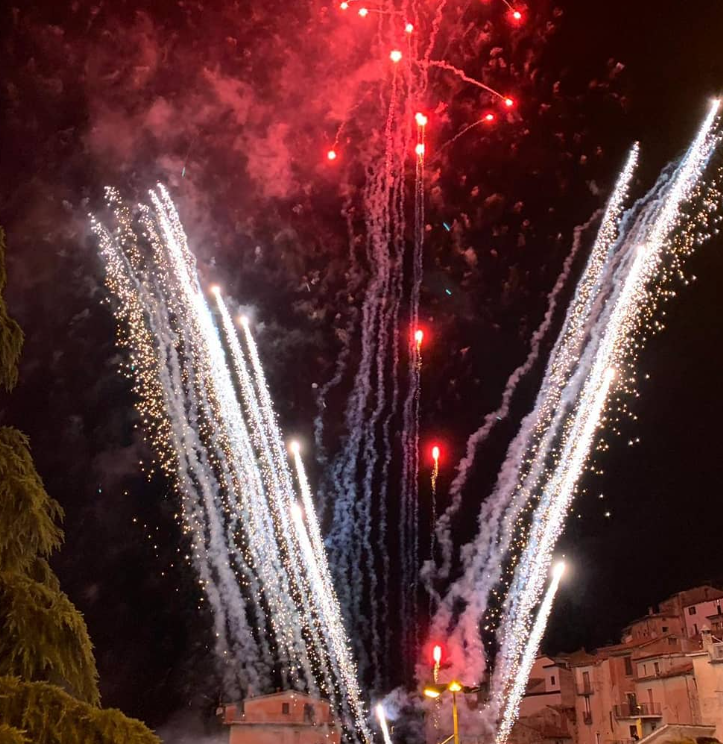 Spettacolo pirotecnico notturno con fuochi d'artificio bianchi e rossi su una città contro un cielo scuro.