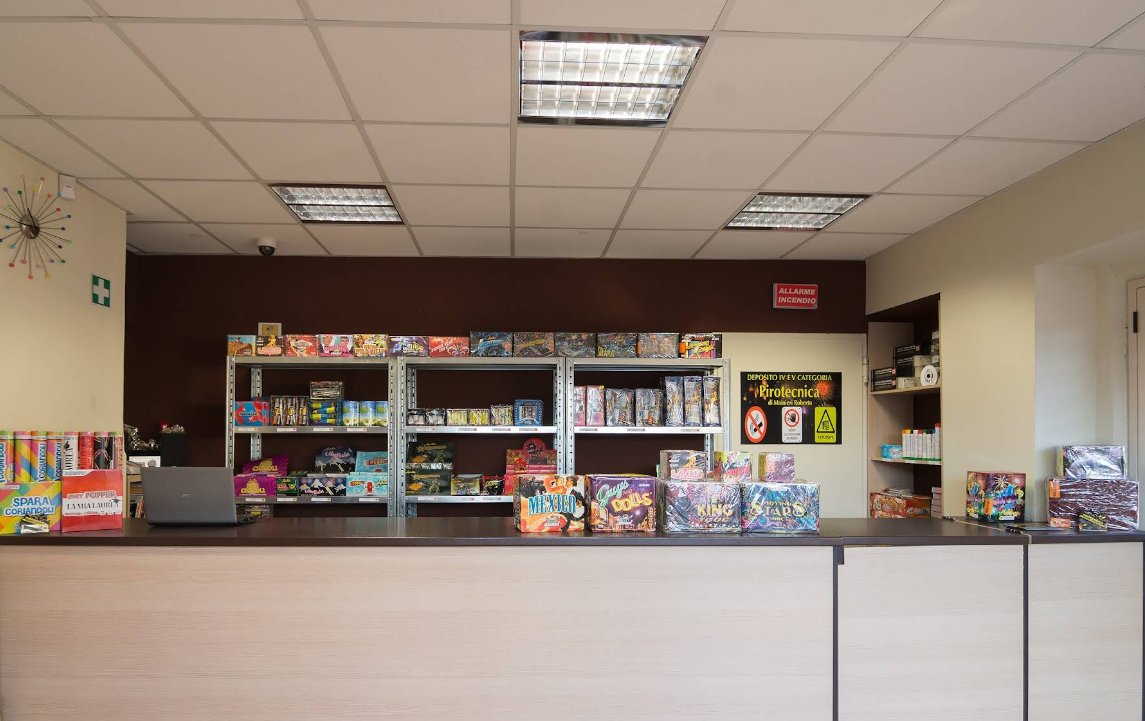 Interno di un negozio al dettaglio con bancone e scaffali pieni di articoli, illuminazione dall'alto.