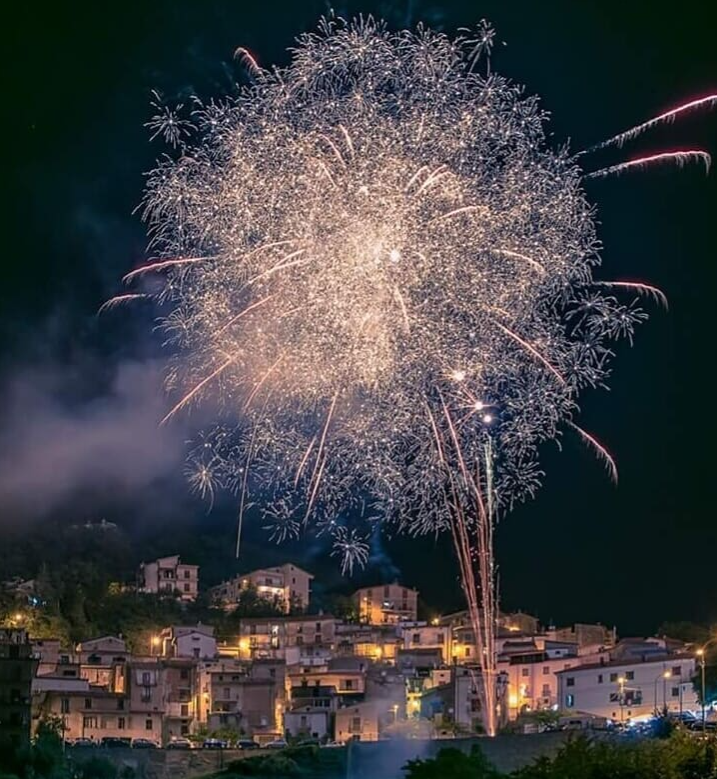 Di notte, i fuochi d'artificio esplodono su una piccola città, illuminando gli edifici con luci bianche e colorate.