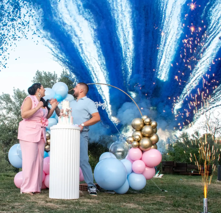 Coppia alla rivelazione del sesso del nascituro, fumo blu che esplode sopra di loro. Palloncini, torta e bengala in un'area verde.
