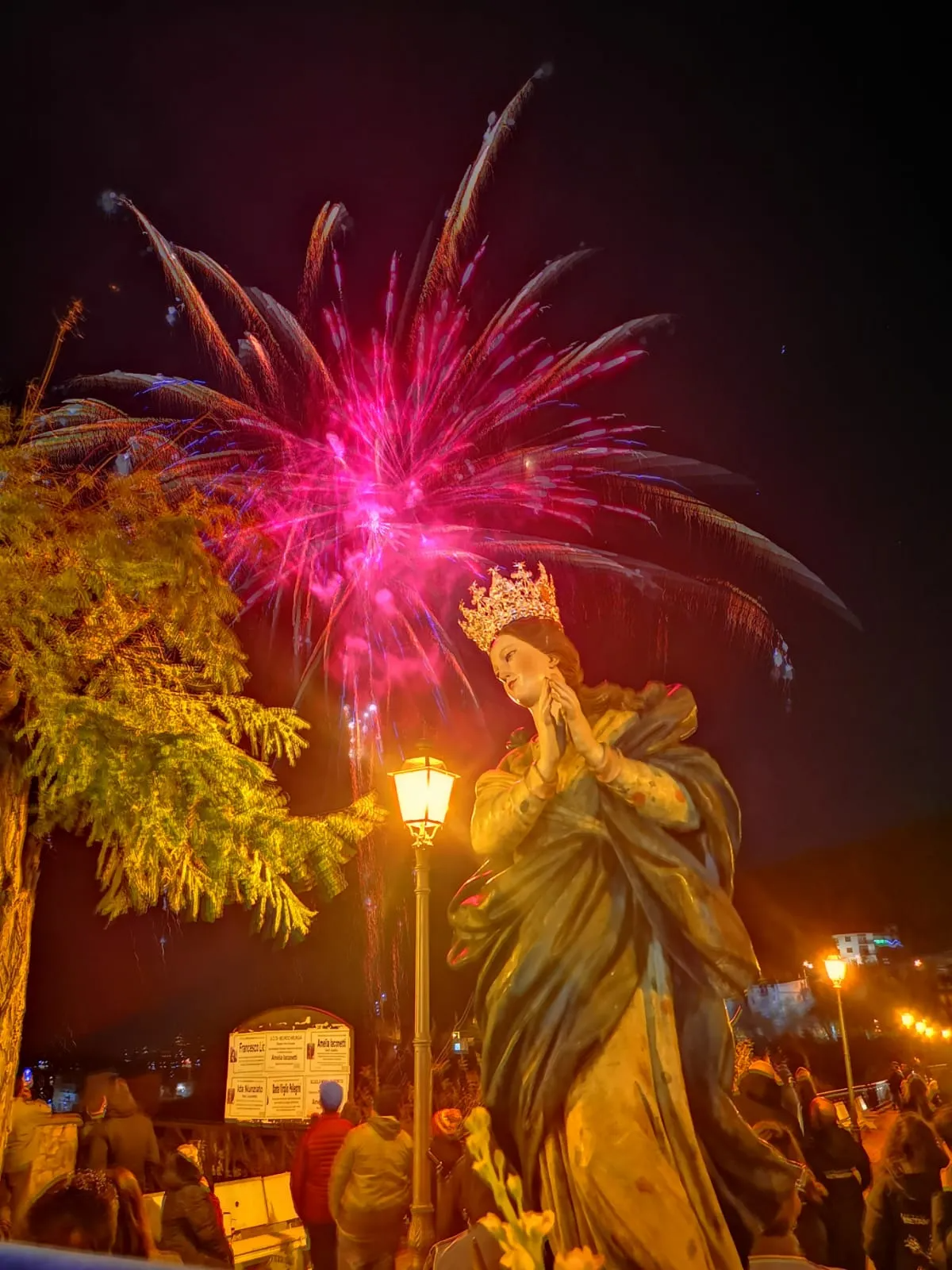 Statua di una donna con corona e fuochi d'artificio nel cielo notturno.