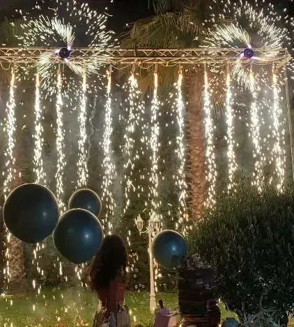 Spettacolo pirotecnico con scintille che scendono e palloncini scuri davanti a una persona.