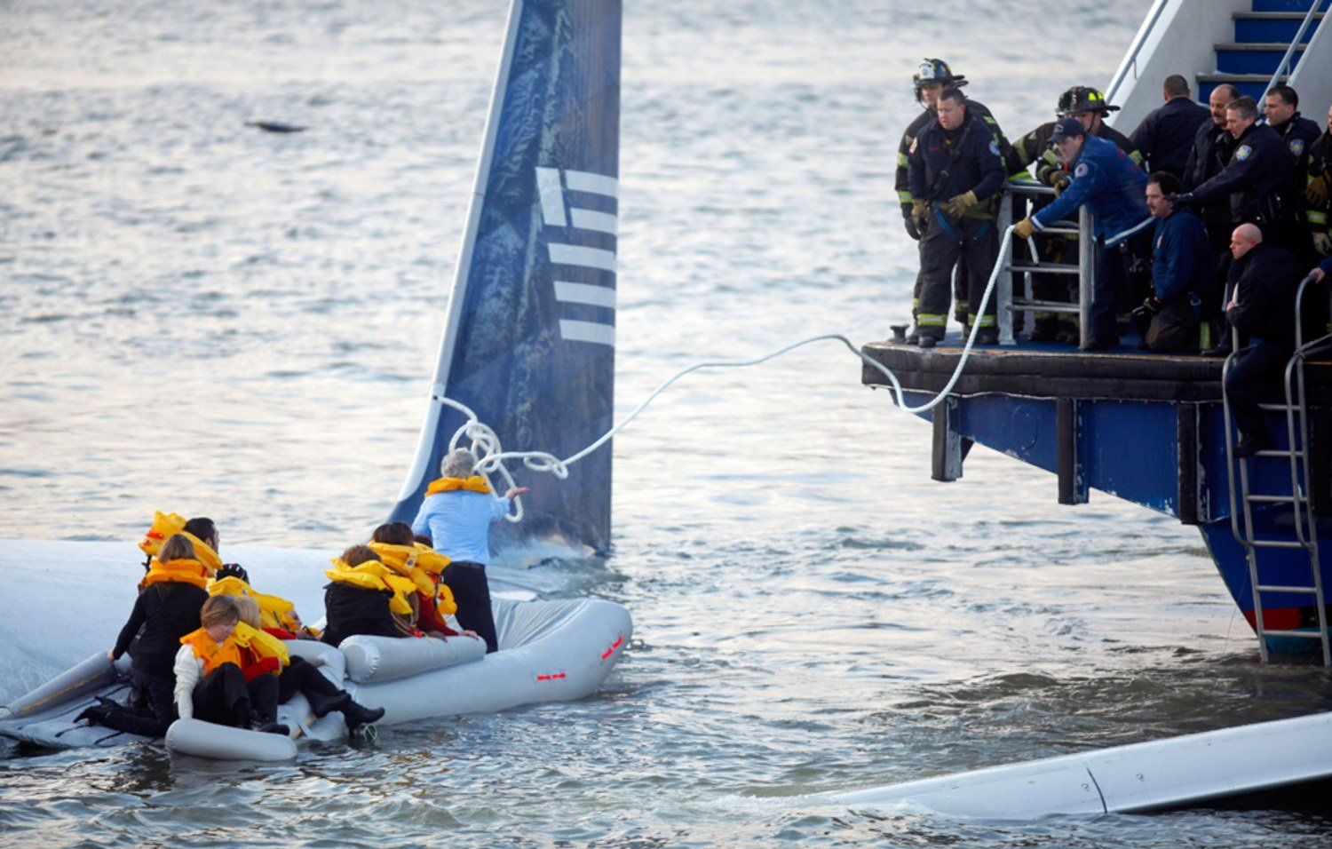 A group of people in life jackets are being pulled out of the water by a boat