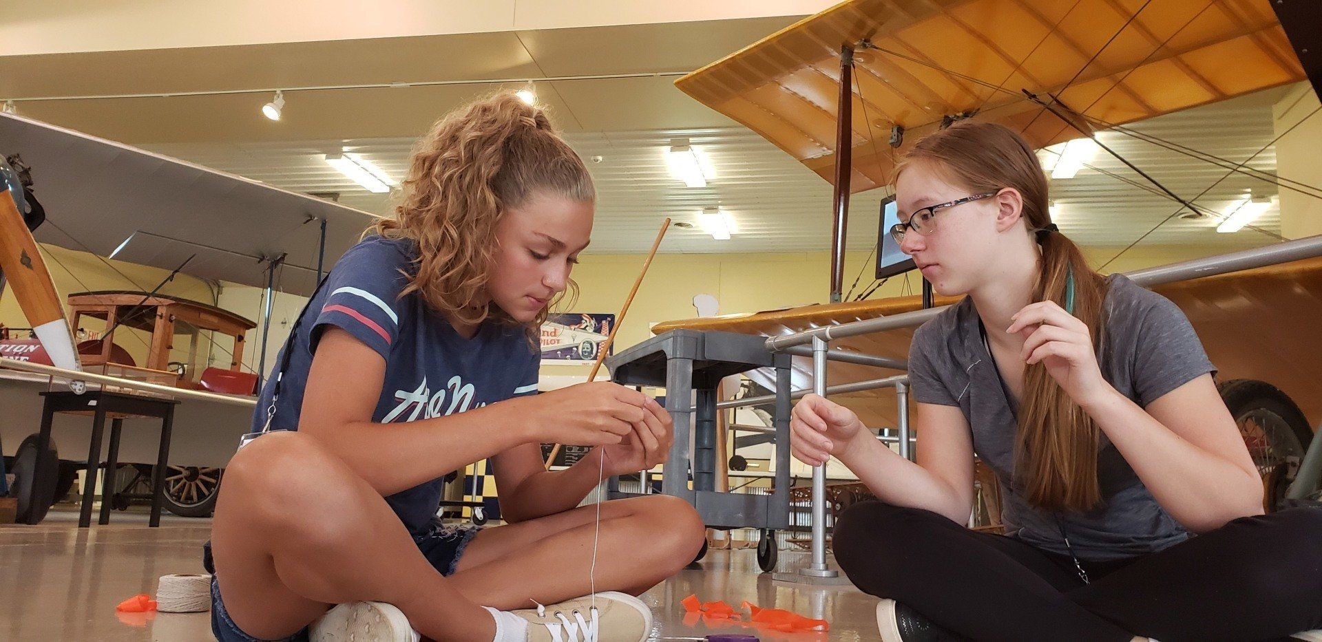 Two young girls are sitting on the floor working on a project.