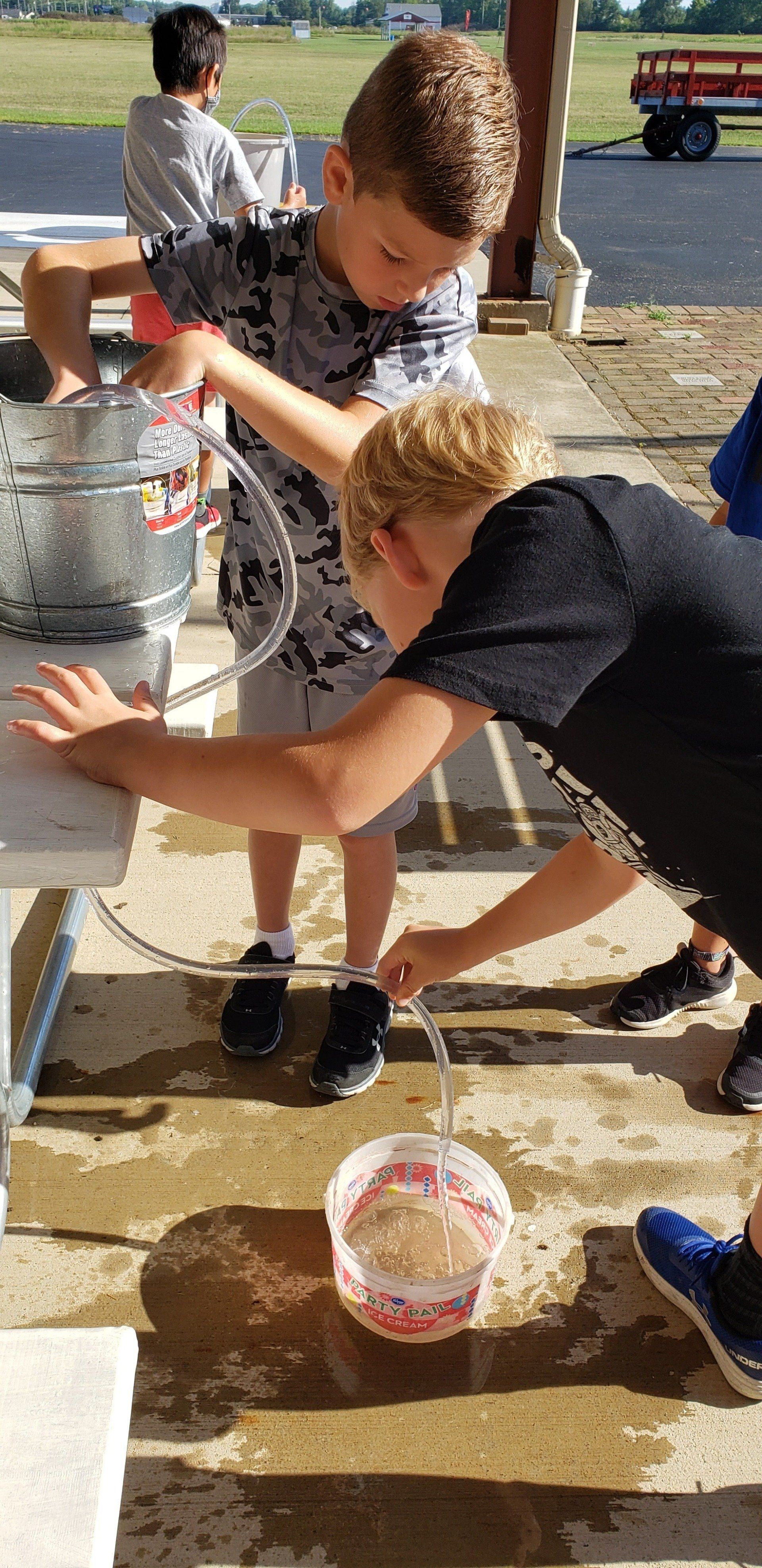 Two young boys are playing with a hose and a bucket of water.