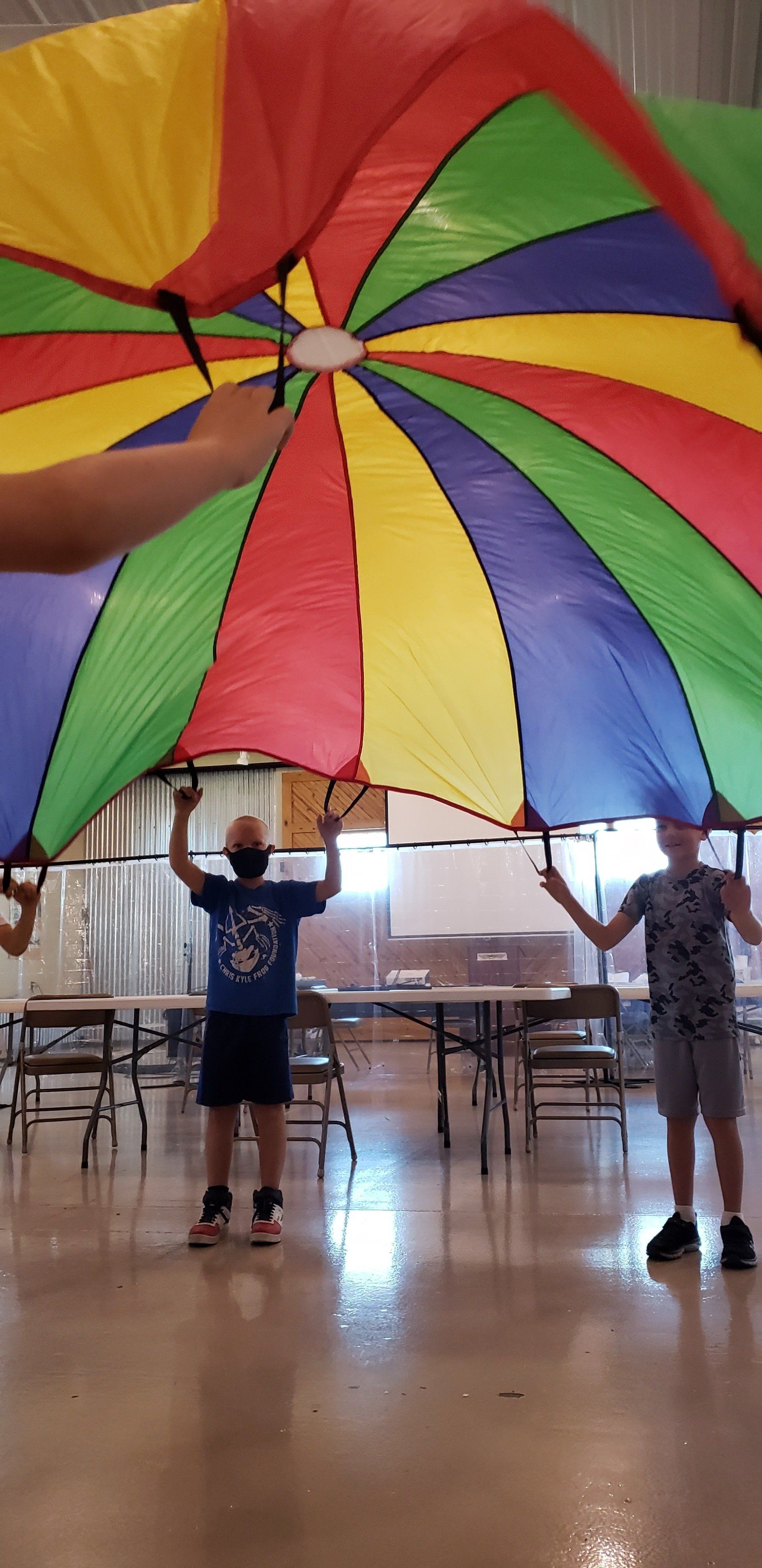 A group of people are holding a colorful parachute in a room.