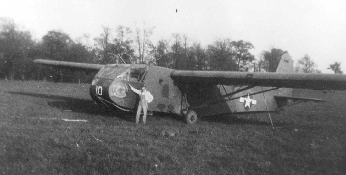 A black and white photo of a man standing next to a plane in a field.