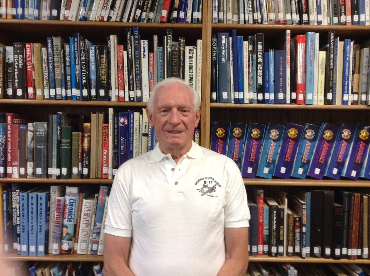 A man in a white shirt stands in front of a bookshelf full of books