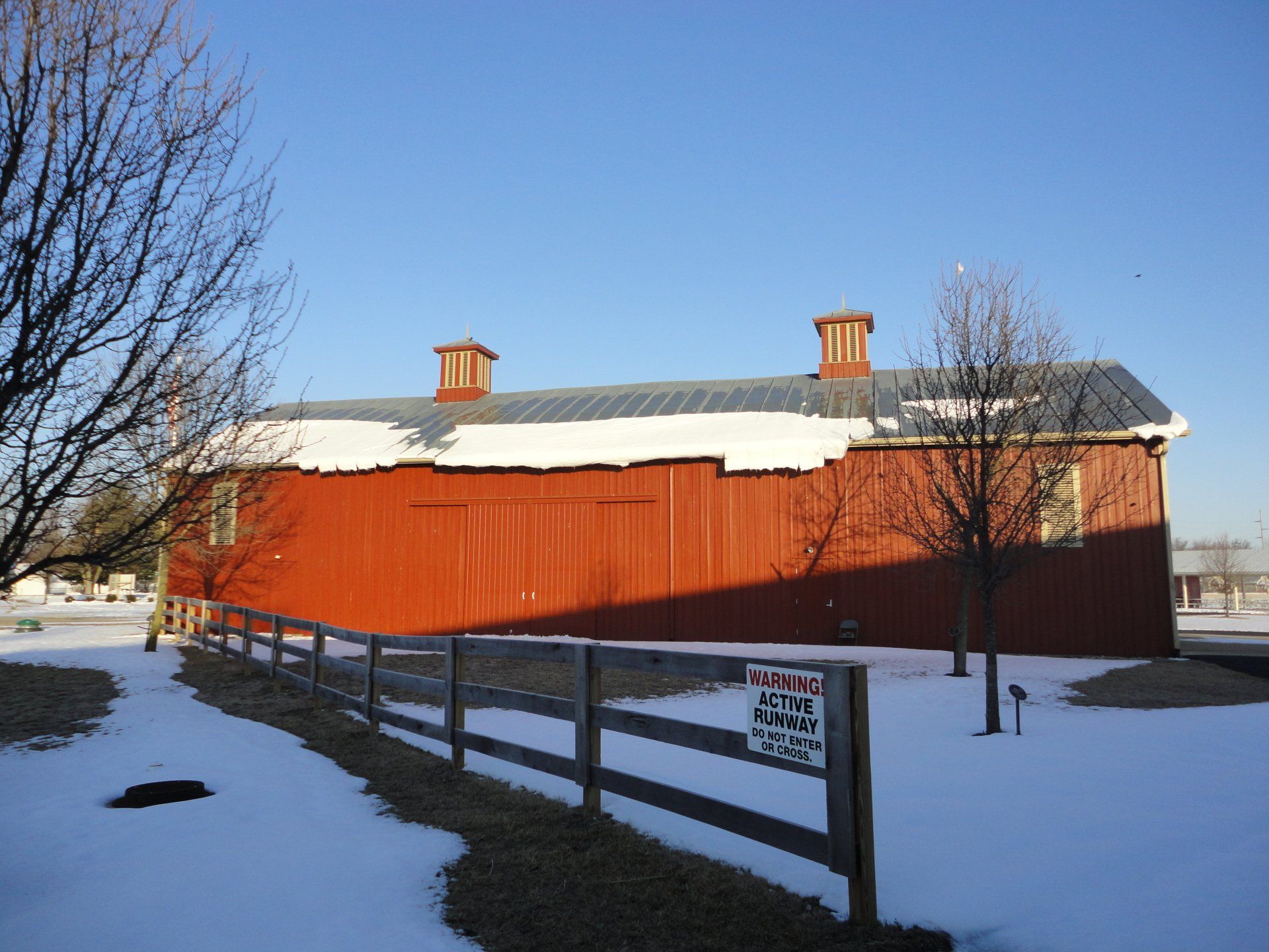 A red barn is surrounded by snow and a wooden fence