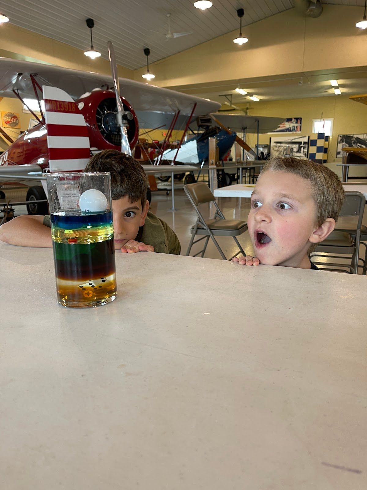 Two young boys are looking at a glass of liquid on a table.