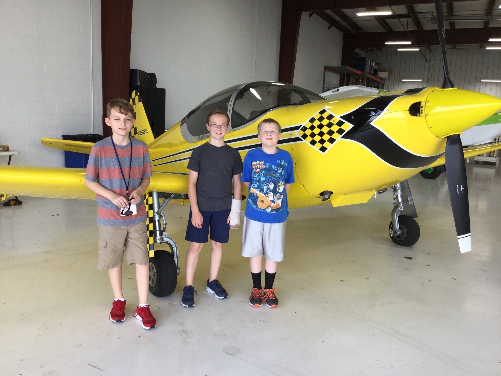 Three young boys are standing in front of a yellow plane