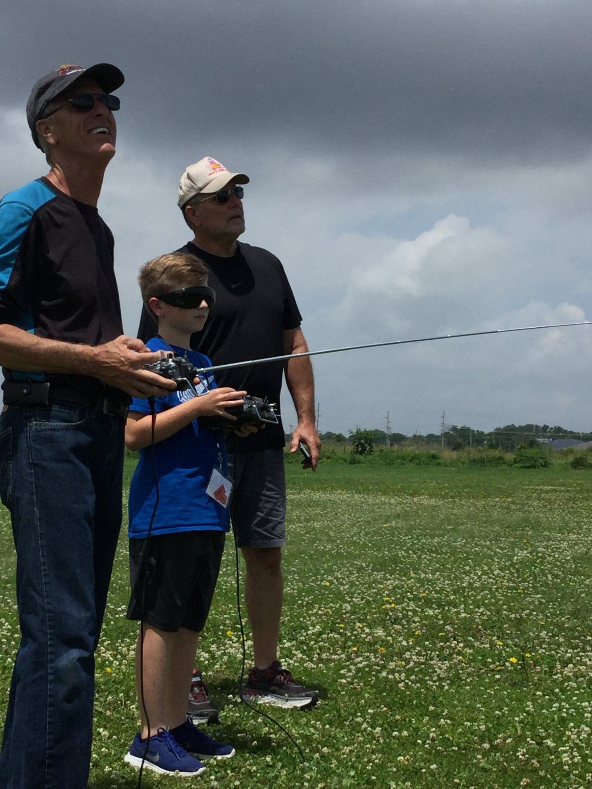 Two men and a boy are playing with a remote control in a field