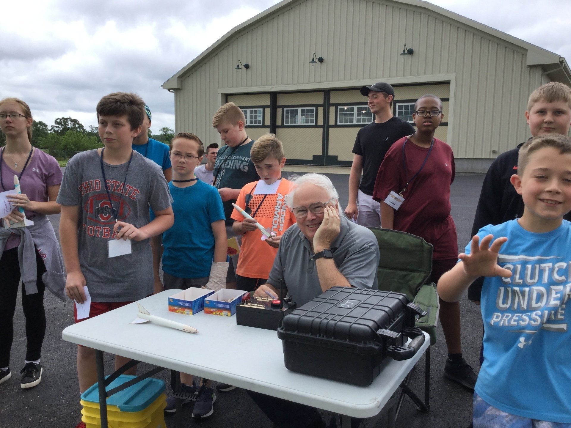 A group of people are standing around a table with a man wearing a blue shirt that says elite under pressure