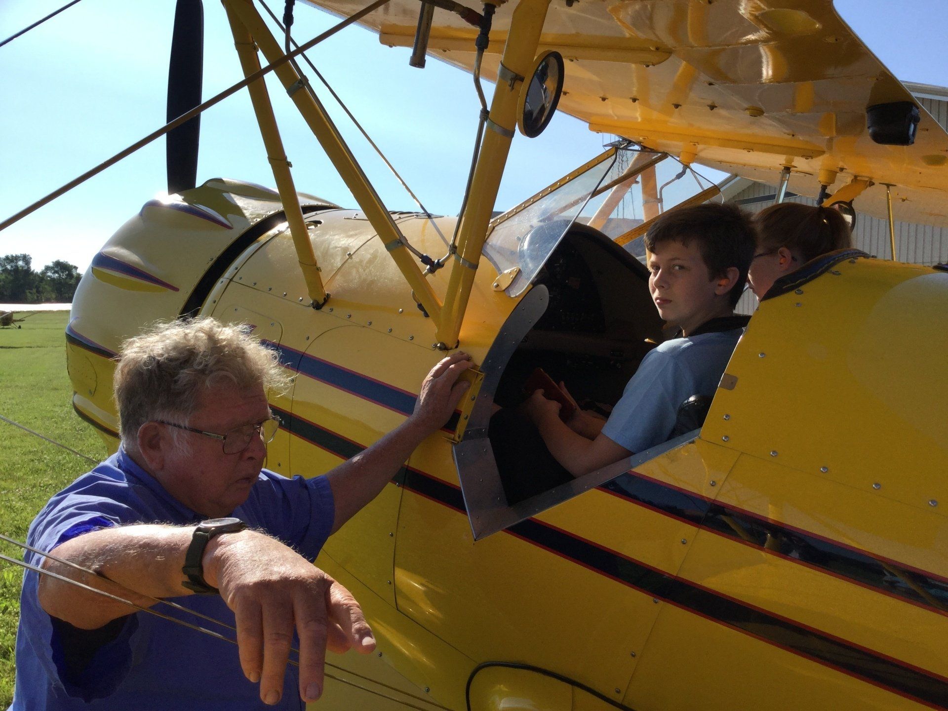A man in a blue shirt is pointing at a yellow airplane