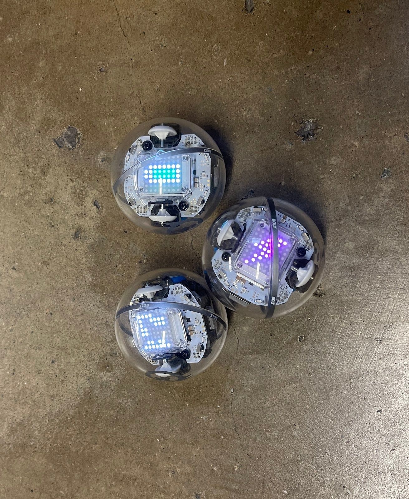 Three robots are sitting on a concrete surface.