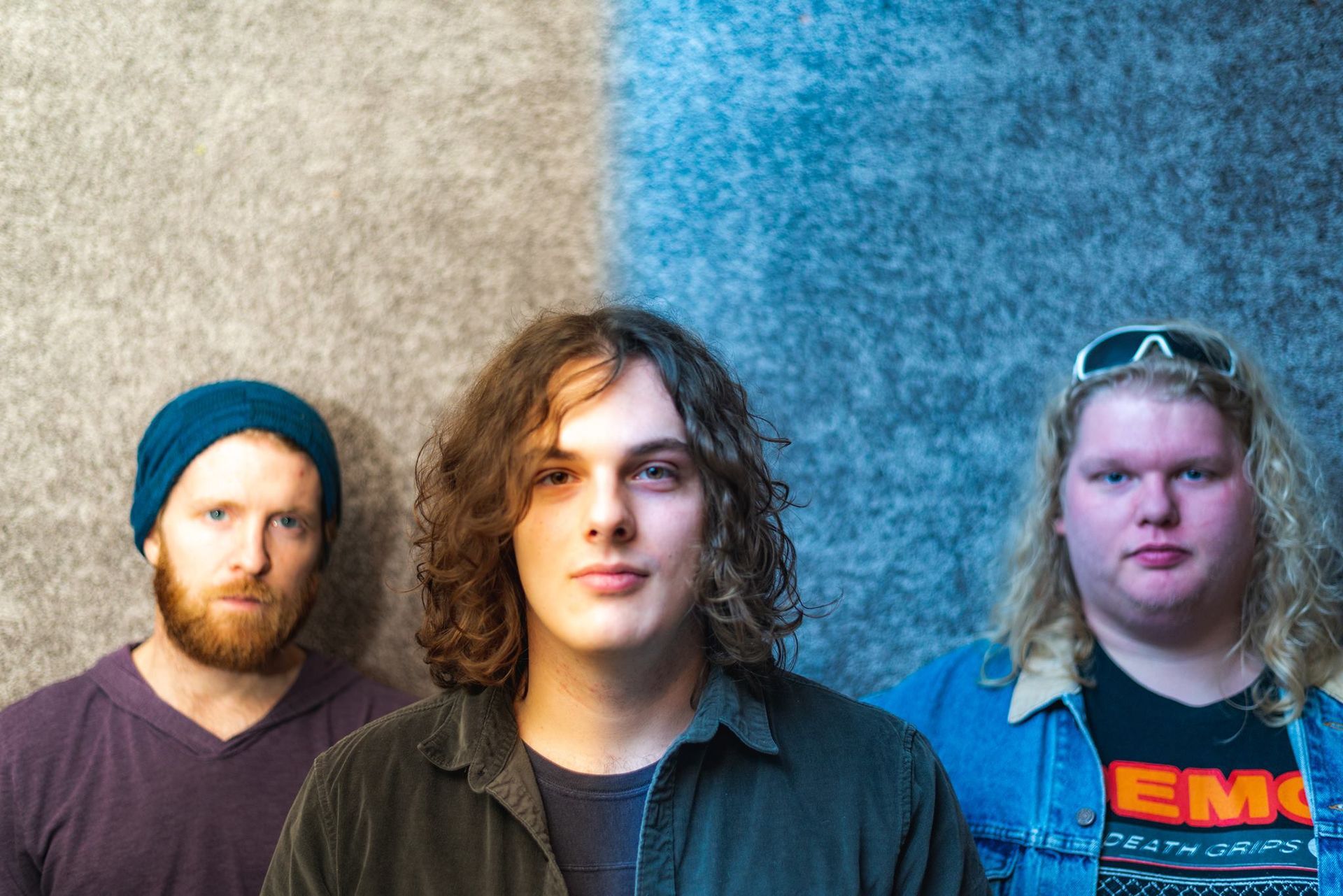 Three men are standing next to each other in front of a blue wall.