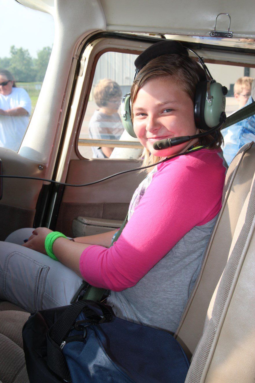 A young girl wearing headphones is sitting in the back seat of a plane.