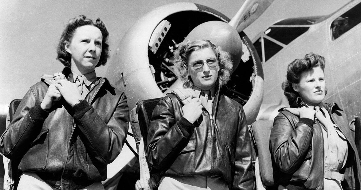 Three women in leather jackets are standing in front of an airplane.