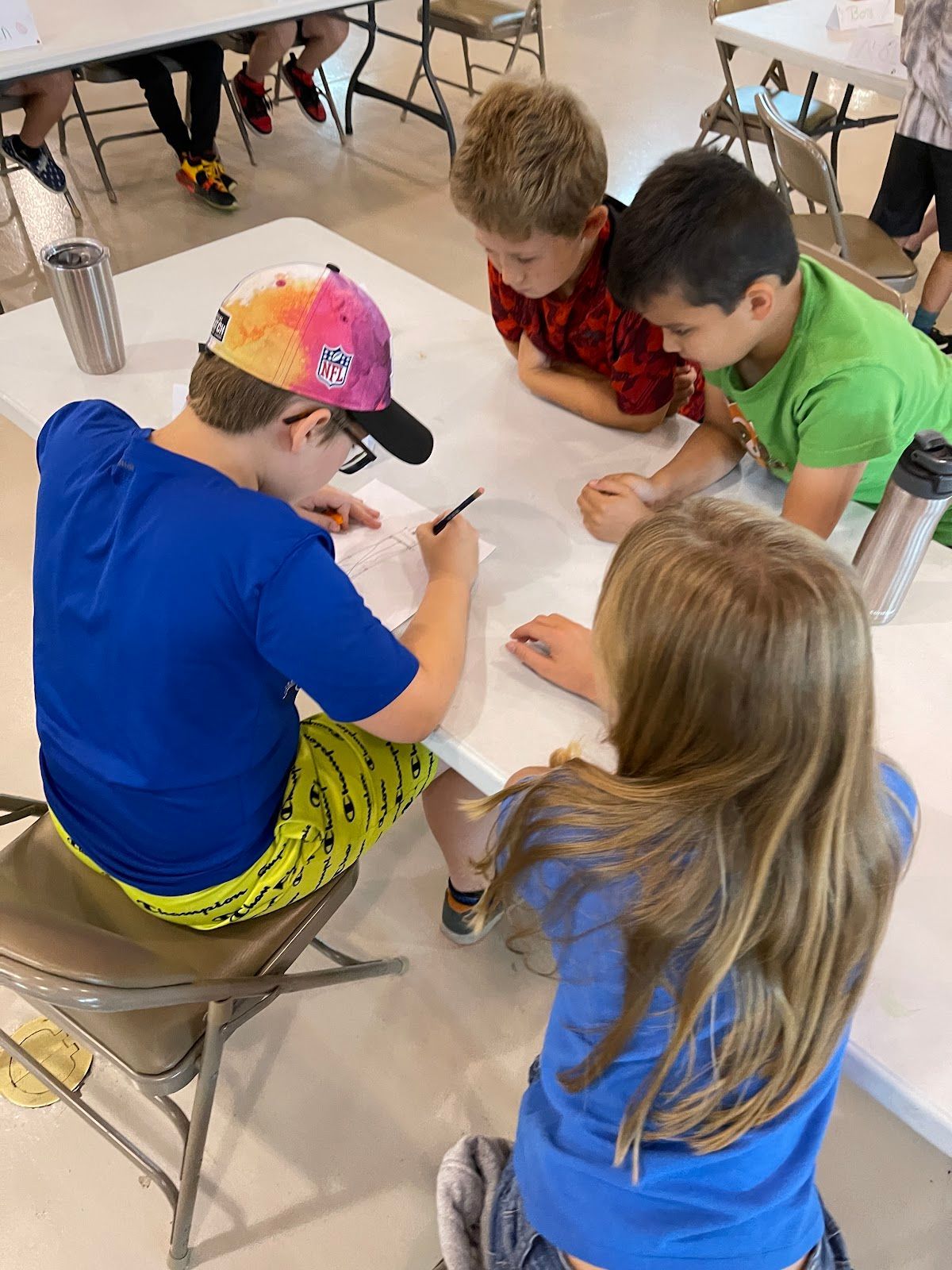 A group of children are sitting at a table writing on a piece of paper.
